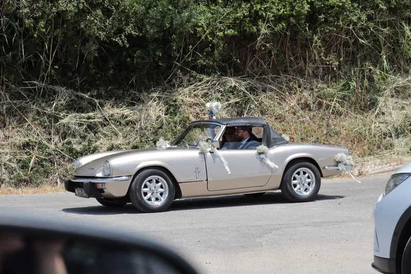 Noivos no Triumph Spitfire decorado com flores numa estrada